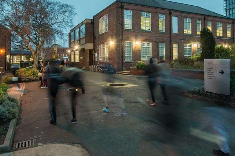 Long exposure image of people walking along a street with University buildings surrounding them.