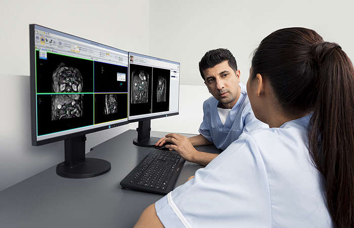 A radiographer from Elekta Unity planning a consultation with patient next to computer screens