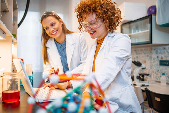 Smiling female scientists in lab coats carrying out physics-based research