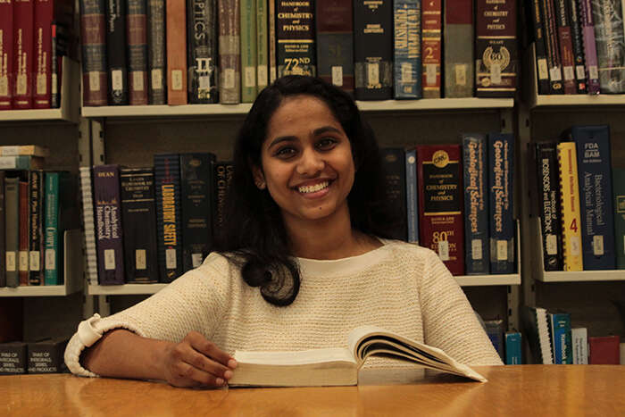 Female physicist Aishwarya Chanady Babu smiling and reading a book