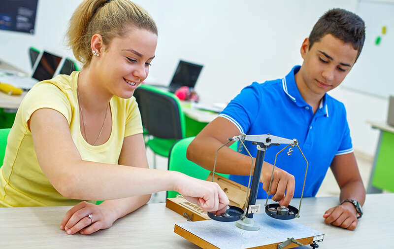 A female and male physics student in the classroom smiling using scales